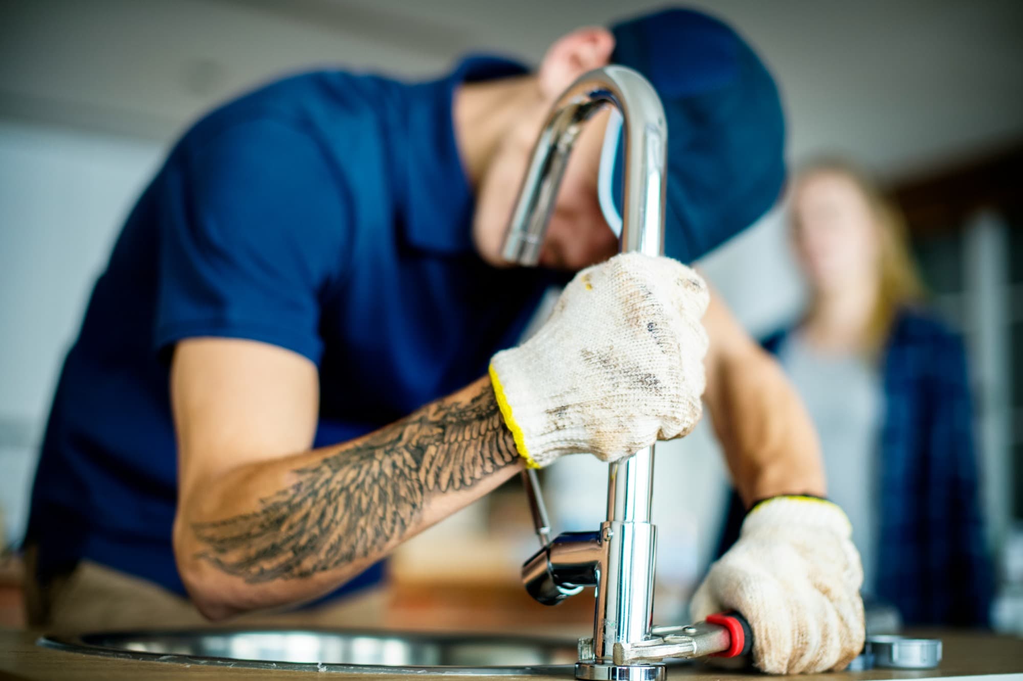 A plumber installing a kitchen faucet in a home.