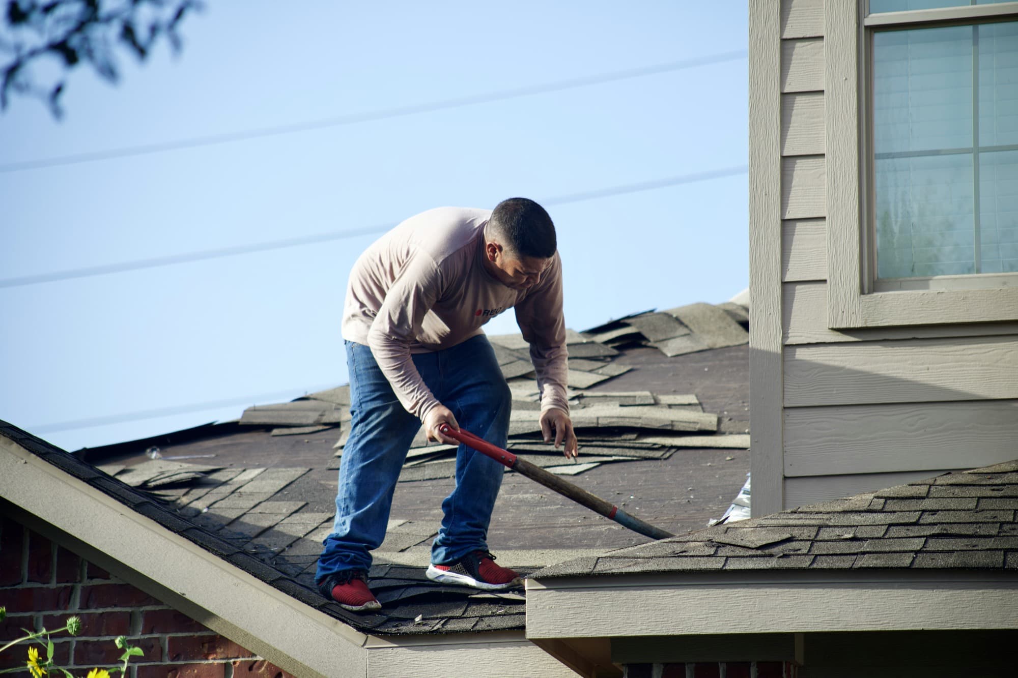 A roofer stripping old shingles from a house.
