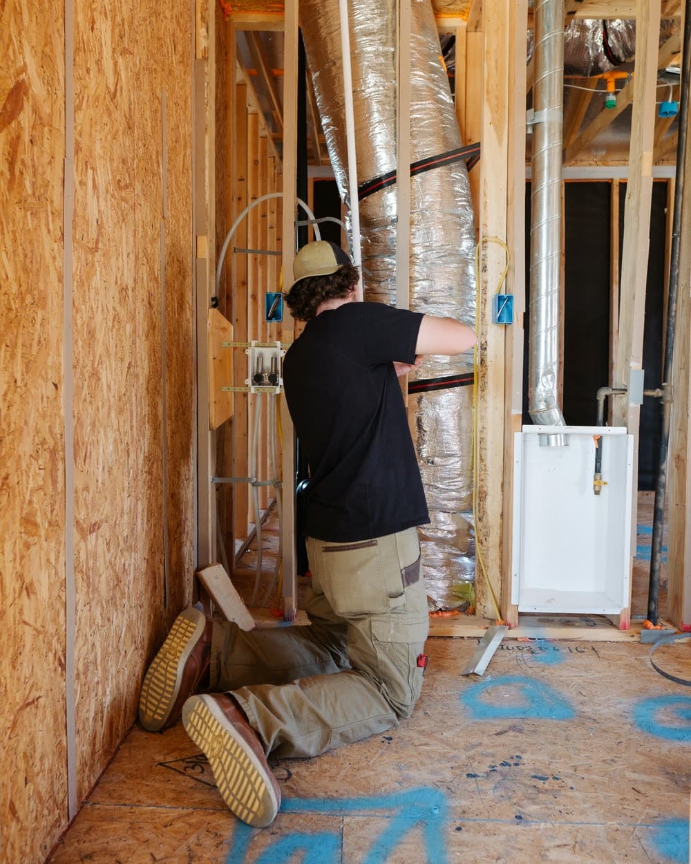 A technician working on ductwork inside a house under construction.