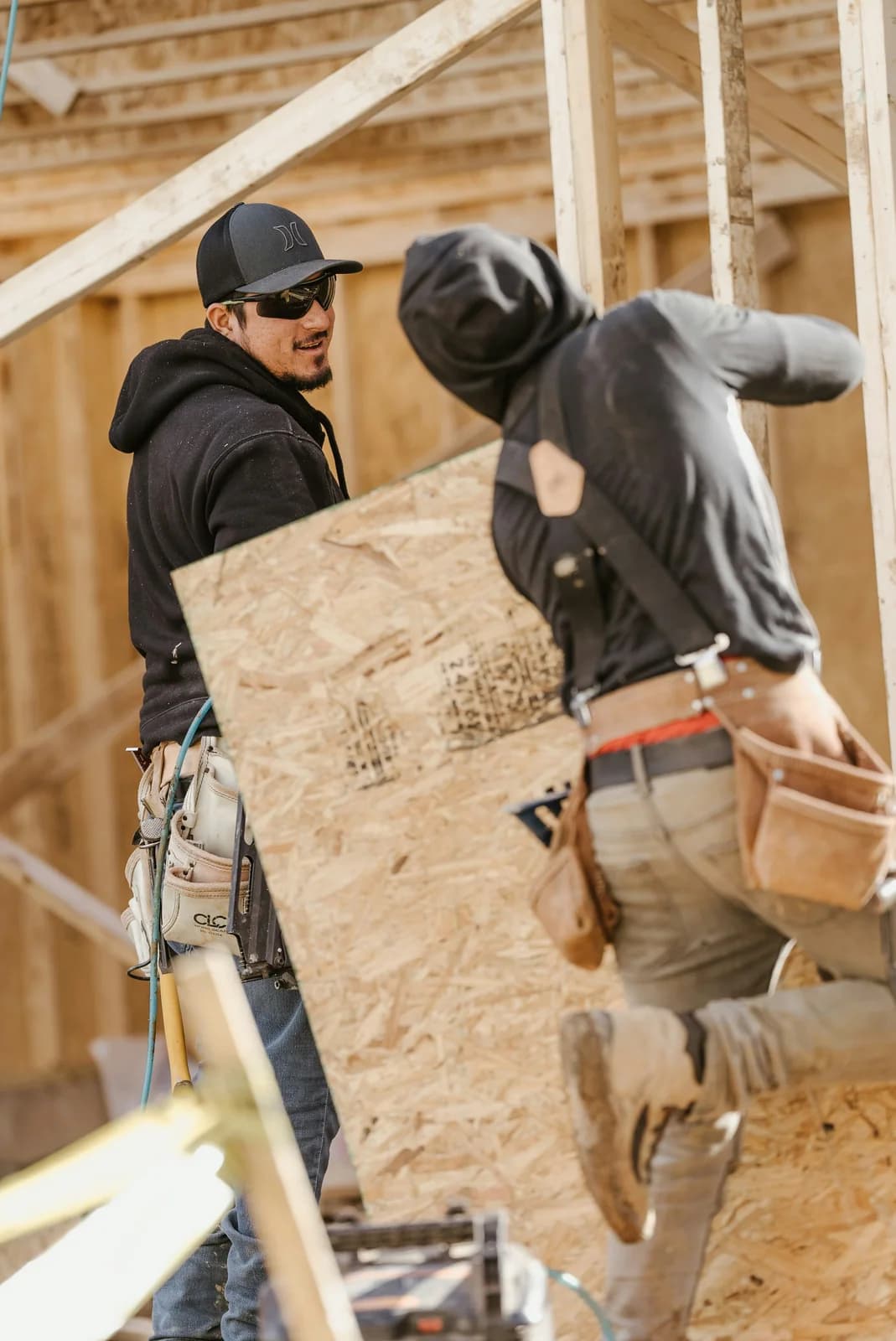 Two crew members carrying a sheet of plywood on a framing job.