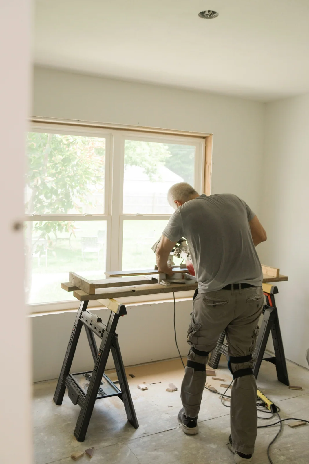 A tradesperson cutting material on sawhorses inside a home.