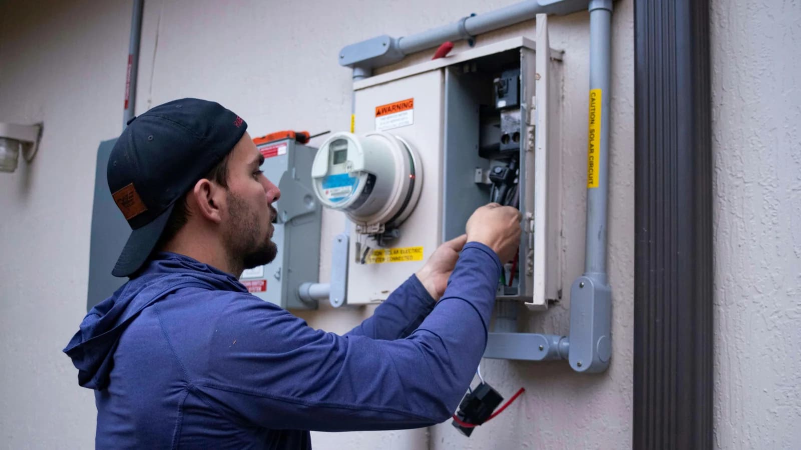 An electrician working at a residential meter and panel.